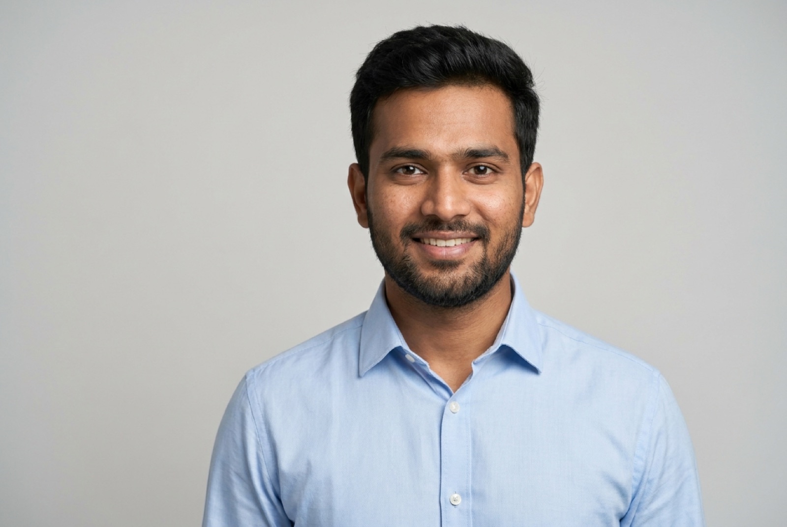 A clean solo head-and-shoulders portrait of a man in a formal light-blue shirt against a plain grey background — an example of a display-picture-ready photo