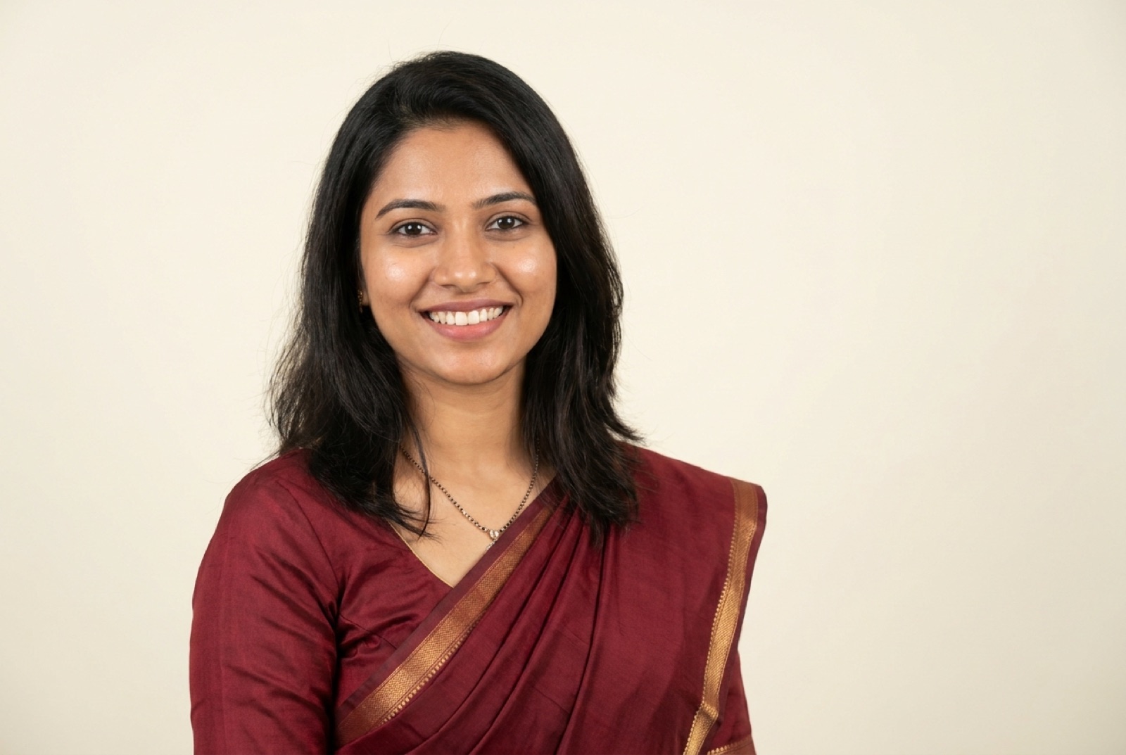 An ideal Shaadi.com profile photo: a woman in a solid maroon saree, head-and-shoulders framing, a warm natural smile, against a plain cream background
